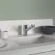 Küchenarbeitsfläche mit einer Ideal Standard Armatur in chrom, einem schwarzen Schalengefäß und weißen Tellern, vor einer grünen Wand.